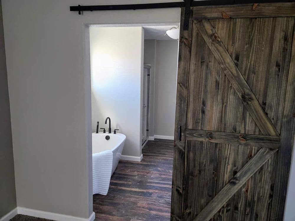 Stylish bathroom entrance with a rustic barn door and vintage bathtub in a modern setting.
