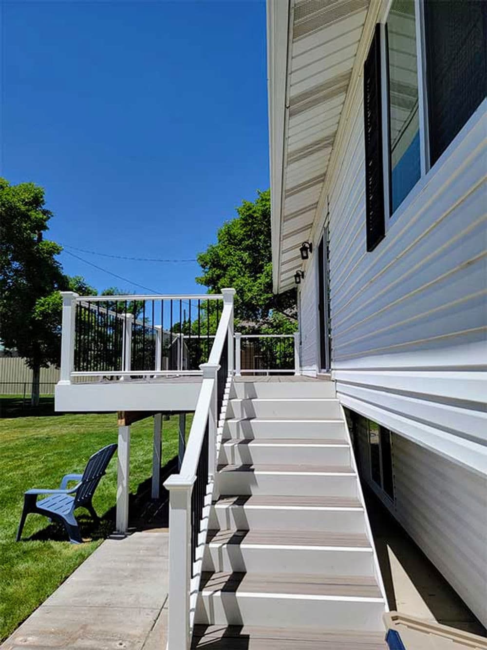 White house exterior with staircase leading to a deck and green lawn under a clear blue sky.